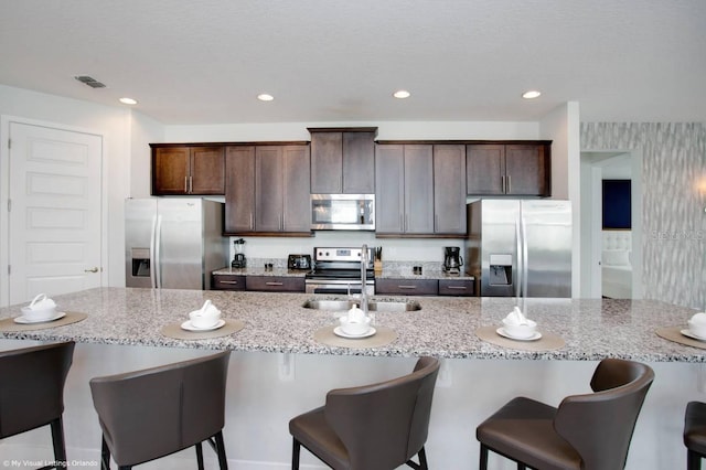 kitchen with appliances with stainless steel finishes, a large island, dark brown cabinetry, sink, and a breakfast bar