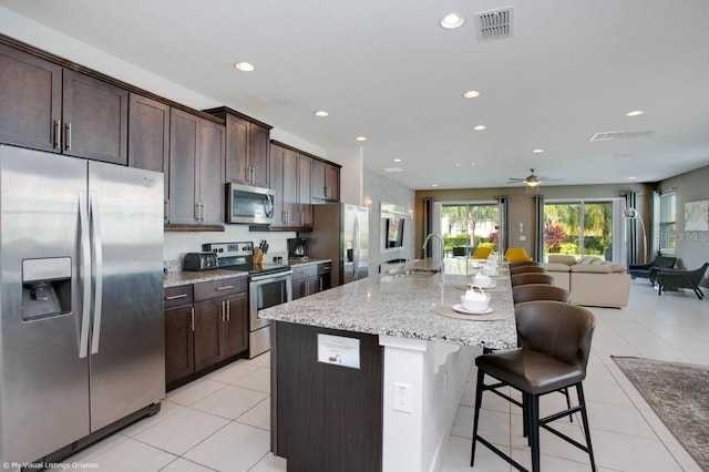 kitchen with a center island with sink, appliances with stainless steel finishes, light stone countertops, sink, and a breakfast bar area