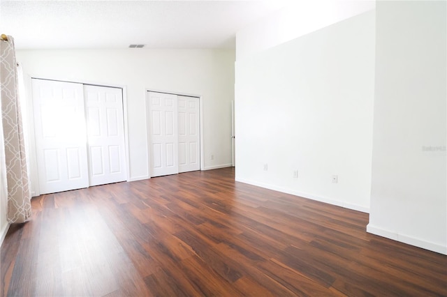 unfurnished bedroom featuring multiple closets, dark wood-type flooring, and vaulted ceiling