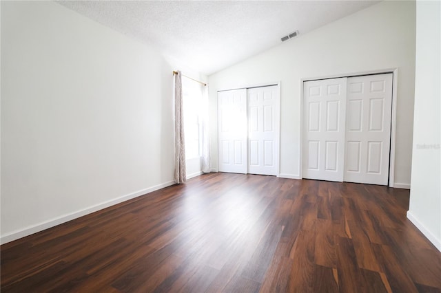 unfurnished bedroom with a textured ceiling, two closets, dark wood-type flooring, and vaulted ceiling