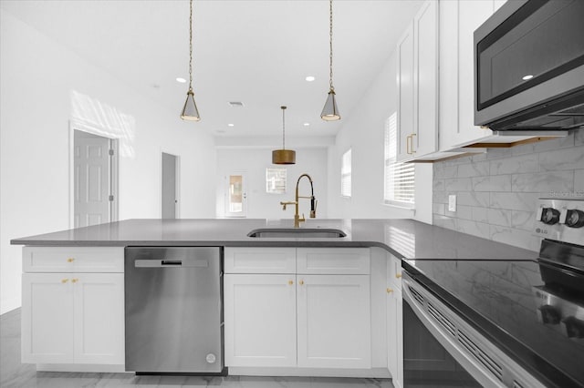 kitchen featuring a peninsula, appliances with stainless steel finishes, white cabinets, and a sink