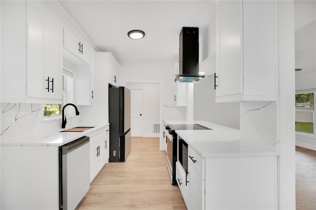 kitchen featuring stainless steel appliances, sink, wall chimney exhaust hood, a healthy amount of sunlight, and white cabinets