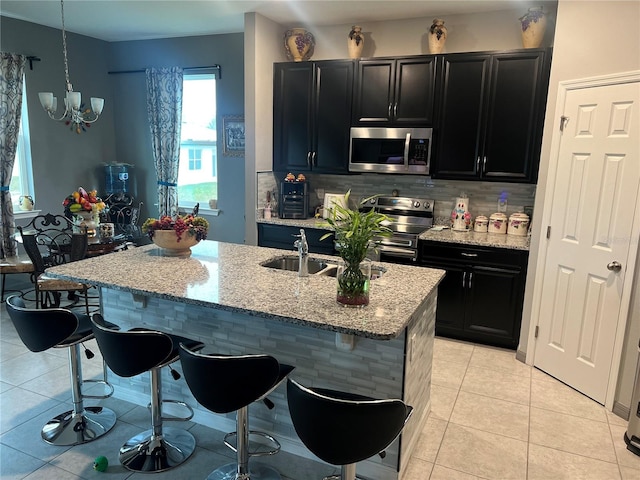 kitchen featuring a center island with sink, appliances with stainless steel finishes, a kitchen breakfast bar, light stone countertops, and an inviting chandelier