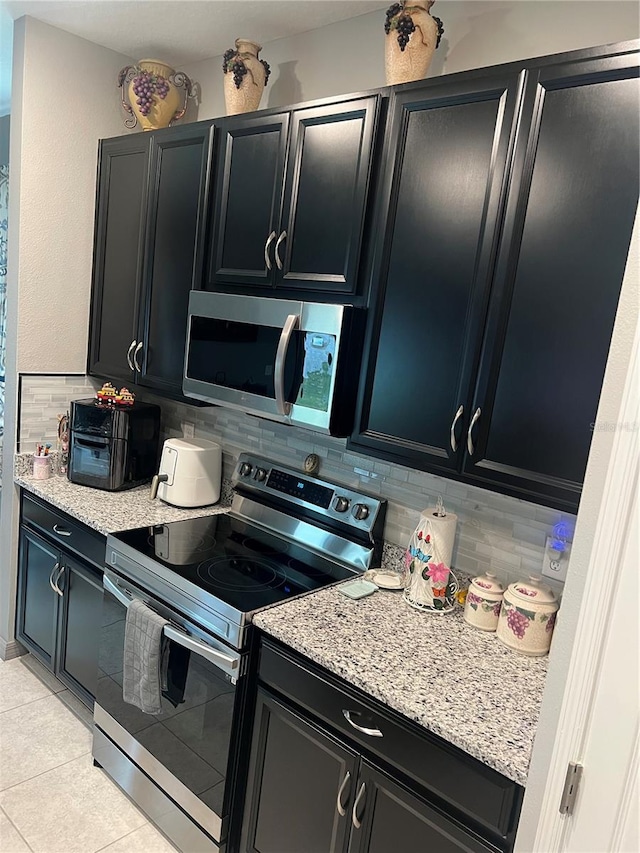 kitchen featuring light stone counters, decorative backsplash, light tile patterned floors, and stainless steel appliances