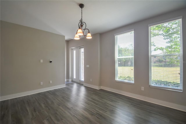 empty room featuring an inviting chandelier, a wealth of natural light, and dark hardwood / wood-style flooring