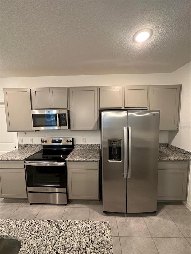 kitchen featuring a textured ceiling, stone countertops, gray cabinetry, and stainless steel appliances