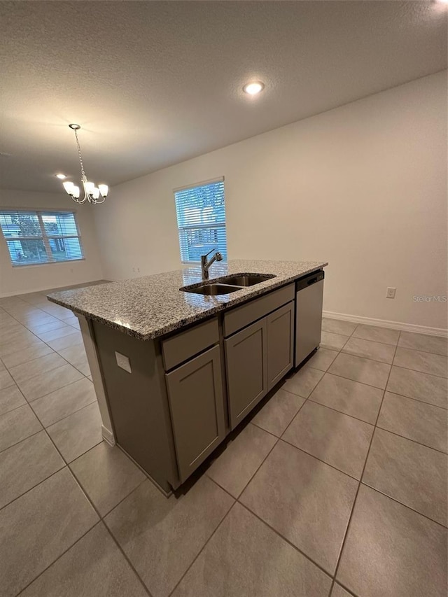 kitchen with pendant lighting, dishwasher, sink, an island with sink, and light stone counters