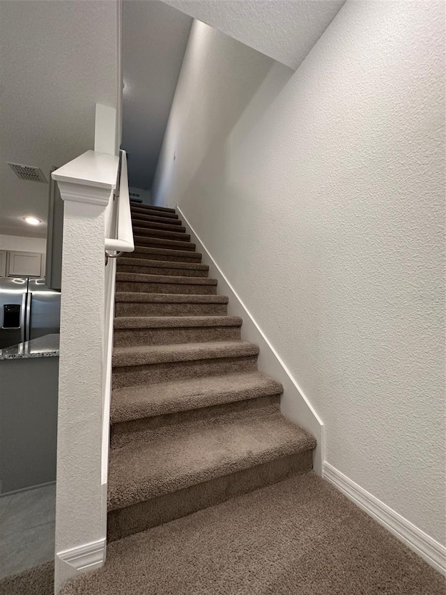 stairway featuring a textured ceiling and carpet floors