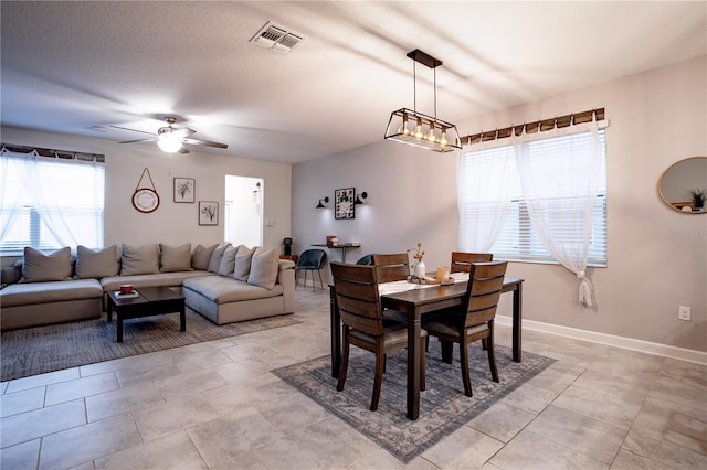 dining space featuring ceiling fan with notable chandelier, plenty of natural light, and a textured ceiling