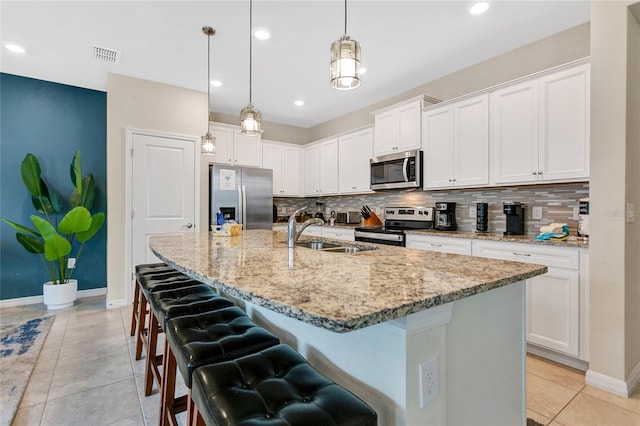 kitchen featuring sink, appliances with stainless steel finishes, an island with sink, white cabinets, and pendant lighting