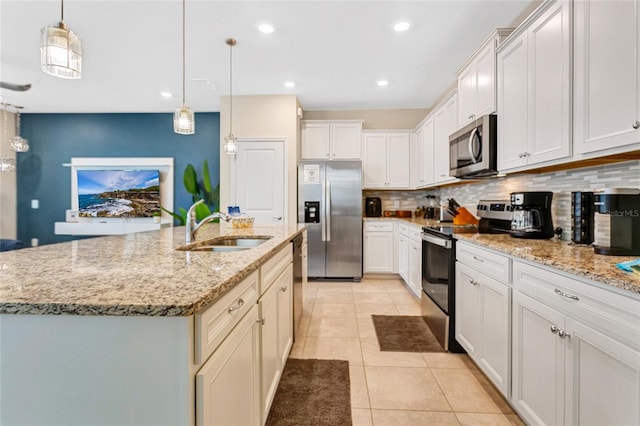 kitchen with stainless steel appliances, a center island with sink, sink, pendant lighting, and white cabinetry