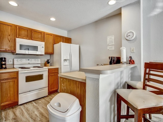 kitchen with light wood-type flooring, kitchen peninsula, a textured ceiling, a breakfast bar, and white appliances