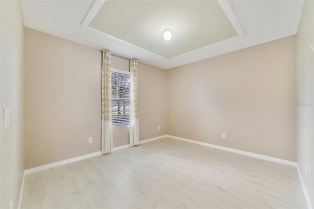 unfurnished room featuring a textured ceiling, light wood-type flooring, and a tray ceiling