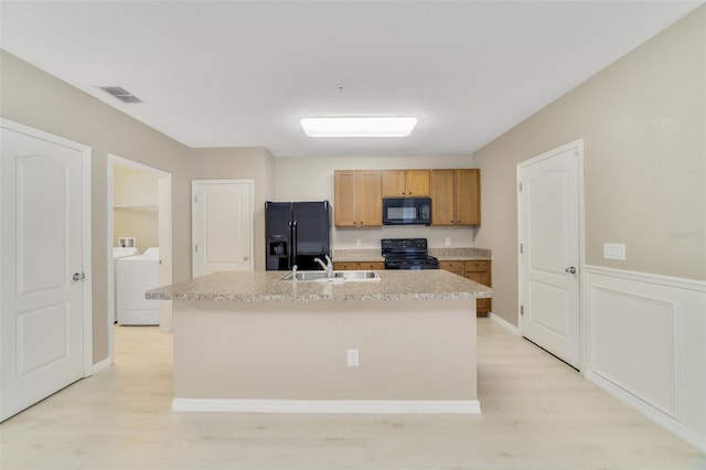 kitchen featuring washing machine and clothes dryer, a kitchen island with sink, sink, and black appliances