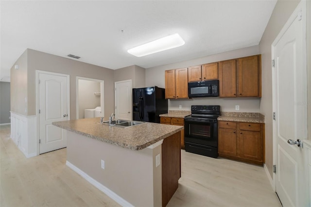 kitchen featuring black appliances, sink, an island with sink, and light hardwood / wood-style flooring