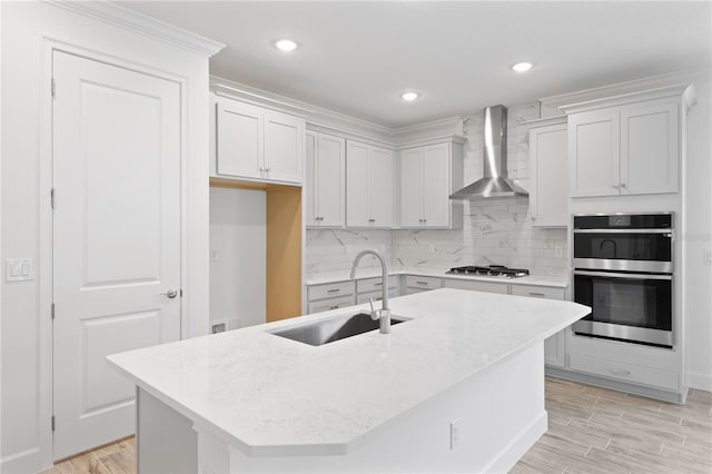 kitchen featuring a kitchen island with sink, appliances with stainless steel finishes, sink, and wall chimney range hood