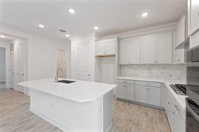 kitchen featuring decorative backsplash, sink, an island with sink, light wood-type flooring, and appliances with stainless steel finishes