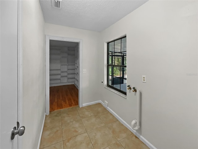 washroom featuring electric dryer hookup, a textured ceiling, and light tile patterned flooring