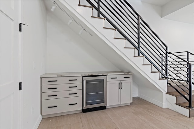 bar with light hardwood / wood-style flooring, beverage cooler, and white cabinets