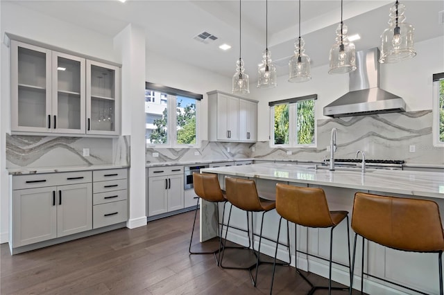 kitchen with dark wood-type flooring, light stone countertops, wall chimney exhaust hood, and a healthy amount of sunlight