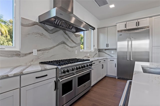 kitchen with dark hardwood / wood-style flooring, decorative backsplash, wall chimney exhaust hood, high quality appliances, and white cabinetry