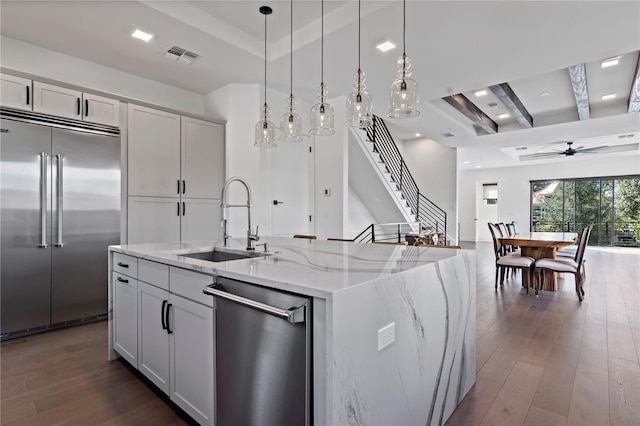 kitchen with stainless steel appliances, sink, light stone countertops, an island with sink, and dark hardwood / wood-style flooring