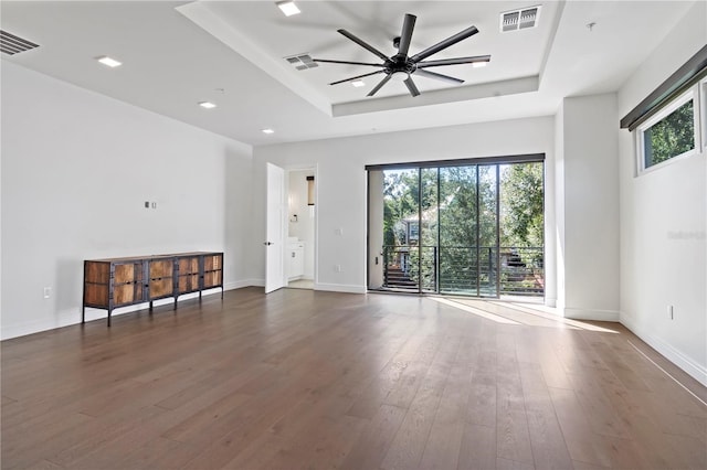 spare room with dark hardwood / wood-style flooring, a healthy amount of sunlight, ceiling fan, and a tray ceiling