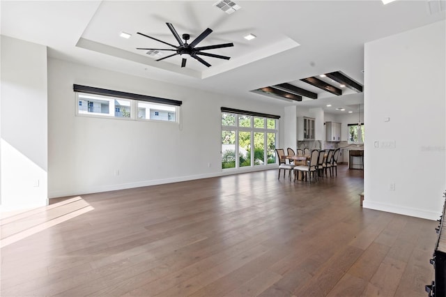 unfurnished living room featuring hardwood / wood-style floors, ceiling fan, and a raised ceiling