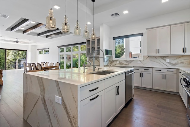 kitchen featuring light stone counters, backsplash, beam ceiling, dark hardwood / wood-style flooring, and an island with sink