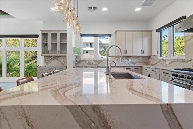 kitchen featuring backsplash, light stone countertops, sink, and decorative light fixtures