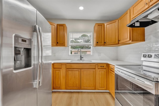 kitchen with tasteful backsplash, stainless steel appliances, sink, and light hardwood / wood-style flooring