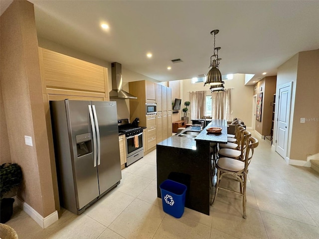 kitchen with stainless steel appliances, wall chimney range hood, sink, an island with sink, and a kitchen breakfast bar