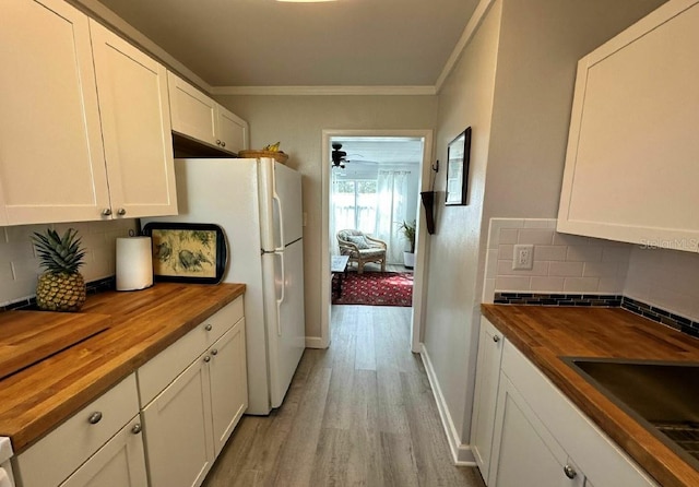 kitchen with white cabinets, ornamental molding, butcher block countertops, and light wood-type flooring