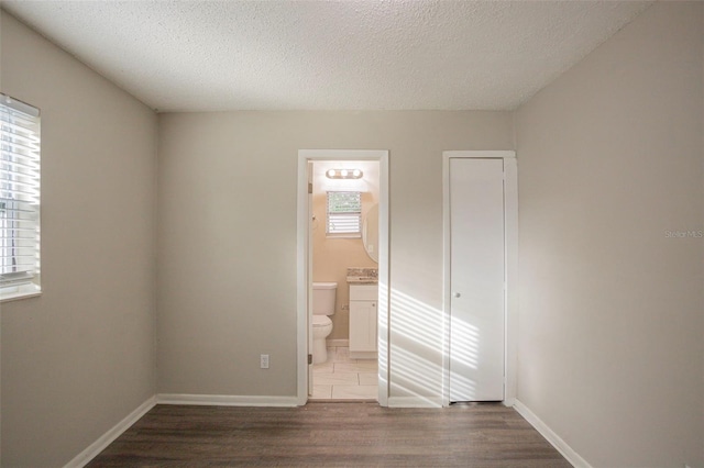 unfurnished bedroom with a textured ceiling, hardwood / wood-style flooring, ensuite bath, and multiple windows