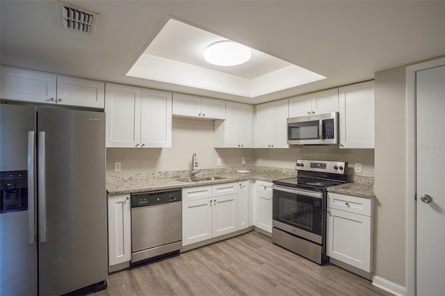 kitchen featuring stainless steel appliances, a tray ceiling, sink, light hardwood / wood-style floors, and white cabinetry