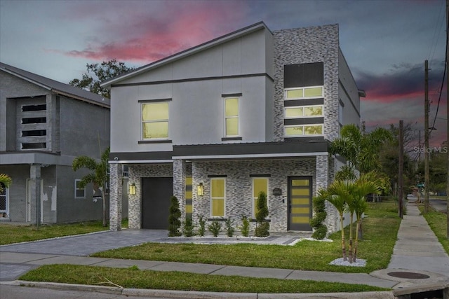 modern home with decorative driveway, an attached garage, a front lawn, and stucco siding