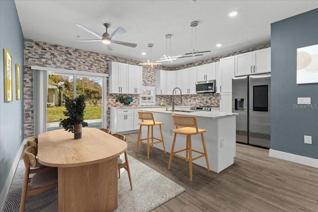 kitchen with a center island with sink, stainless steel appliances, tasteful backsplash, white cabinets, and a sink