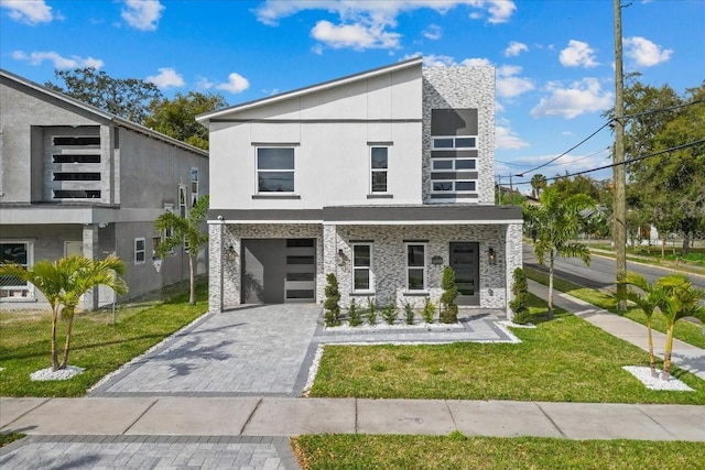 contemporary home featuring an attached garage, stone siding, decorative driveway, stucco siding, and a front lawn