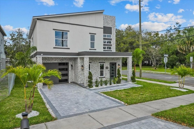 contemporary house featuring an attached garage, stucco siding, decorative driveway, and a front yard