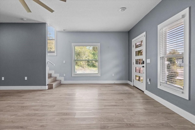 interior space featuring baseboards, a textured ceiling, light wood finished floors, and stairs