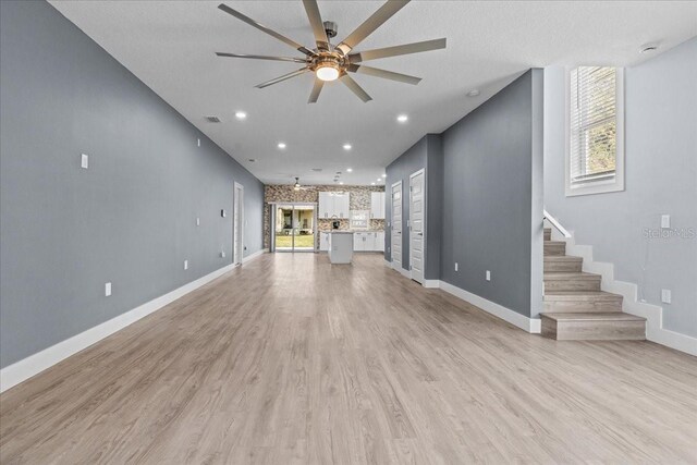 unfurnished living room featuring visible vents, stairway, light wood-style flooring, a ceiling fan, and baseboards