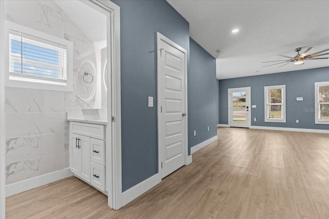 unfurnished living room featuring light wood finished floors, baseboards, and a ceiling fan