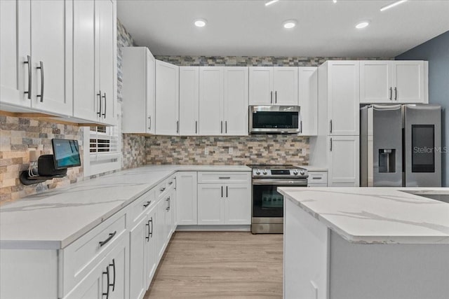 kitchen with light wood finished floors, white cabinets, decorative backsplash, appliances with stainless steel finishes, and light stone countertops