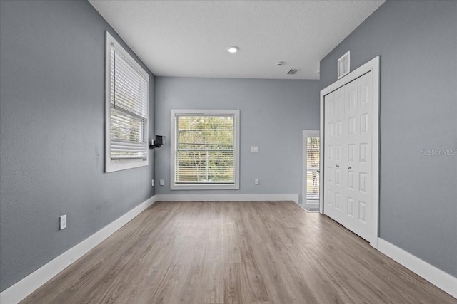 empty room with visible vents, a textured ceiling, baseboards, and wood finished floors