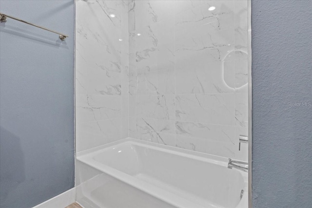 full bathroom featuring a textured wall, baseboards, and shower / bathtub combination