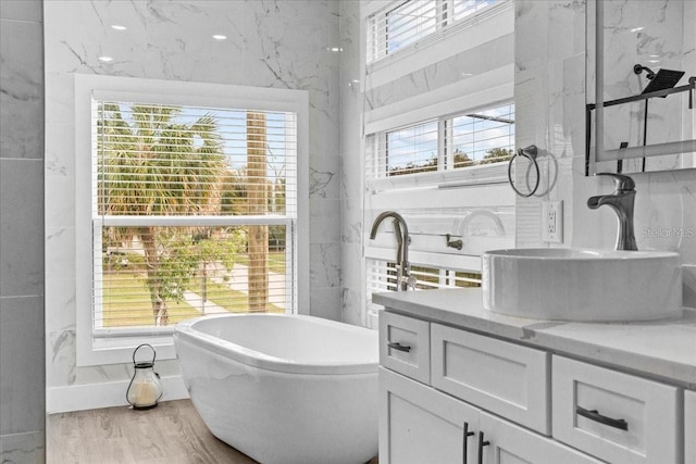 bathroom featuring tile walls, a soaking tub, vanity, and wood finished floors