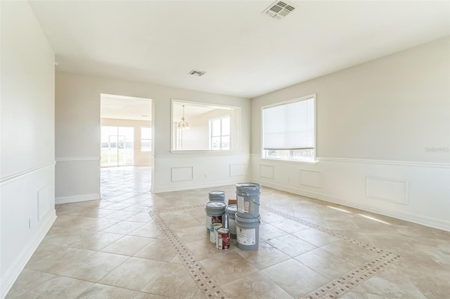 tiled spare room featuring an inviting chandelier