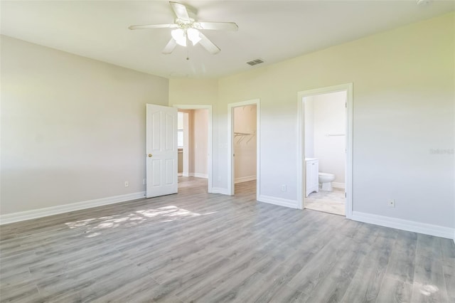 unfurnished bedroom featuring a closet, a spacious closet, light hardwood / wood-style flooring, ceiling fan, and ensuite bathroom