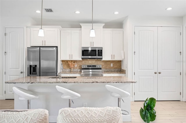 kitchen with an island with sink, white cabinetry, pendant lighting, and appliances with stainless steel finishes