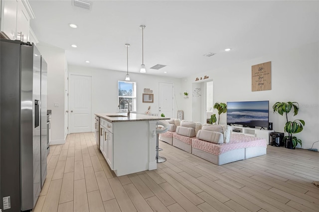 kitchen with white cabinetry, an island with sink, sink, and stainless steel fridge with ice dispenser